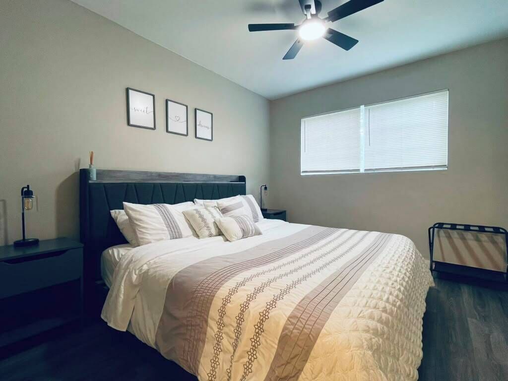 A bedroom with a bed, a nightstand, a ceiling fan, and a window with blinds.