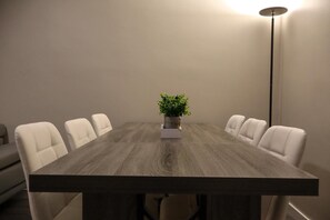 Ein Konferenztisch mit sechs weißen Stühlen, einer Topfpflanze und einer hohen Stehlampe.