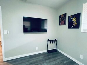 Ein Zimmer mit einem großen Flachbildfernseher an der Wand, einer Klimmzugstange und zwei gerahmten Sportplakaten.