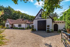 A traditional house with a gravel driveway, a large garage door, and a wooden fence. - 4 Bed in Itchenor (oc-l45314) (Itchenor)
