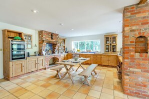 A kitchen with a brick fireplace, wooden cabinets, a double oven, and a dining table with benches. - 4 Bed in Itchenor (oc-l45314) (Itchenor)