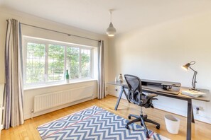 A room with a large window, a desk with a chair, a lamp, and a patterned rug. - 4 Bed in Itchenor (oc-l45314) (Itchenor)