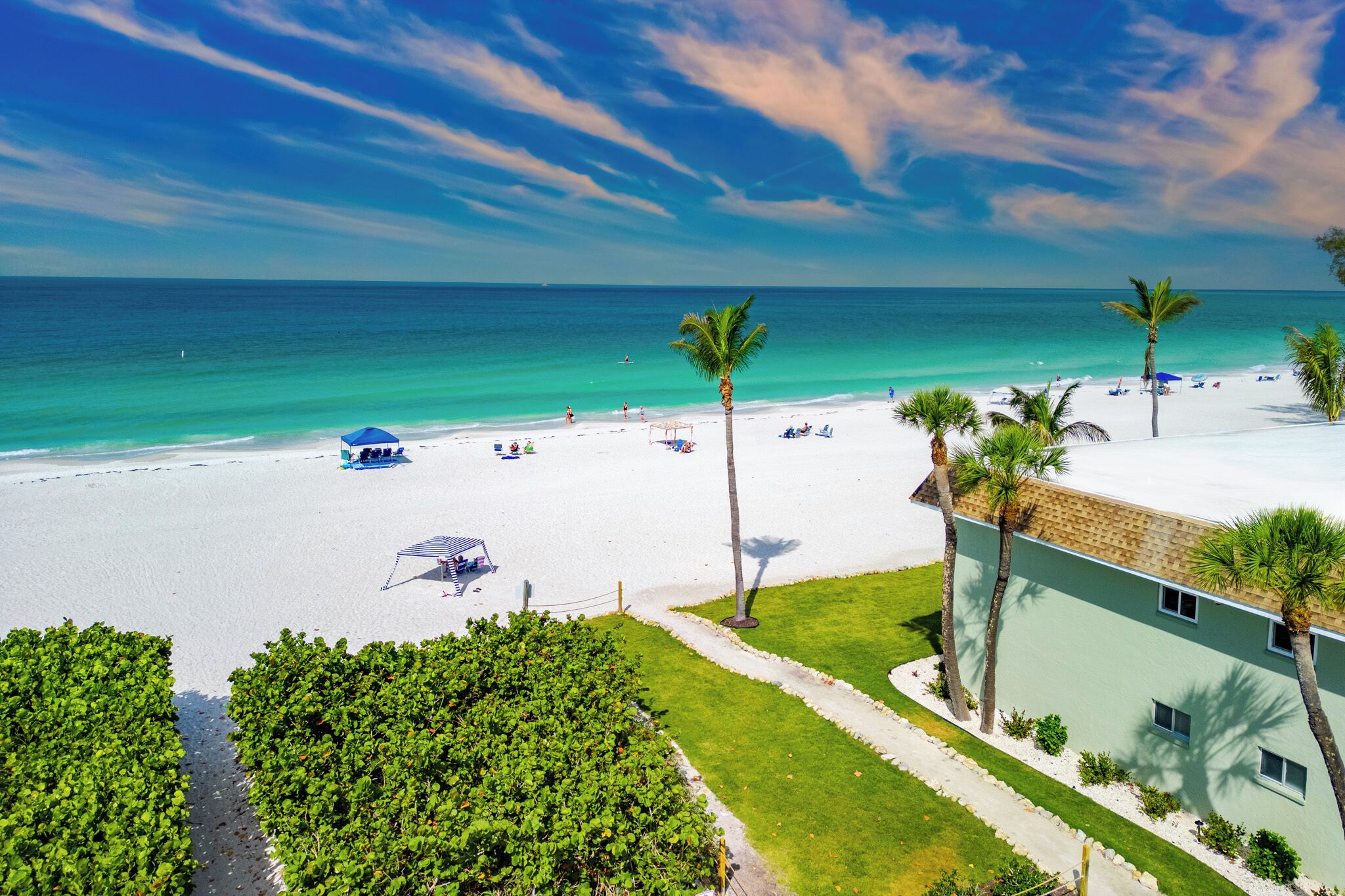 Blick auf einen Strand mit blauem Himmel, feinem Sand und einem Gebäude mit grüner Fassade.