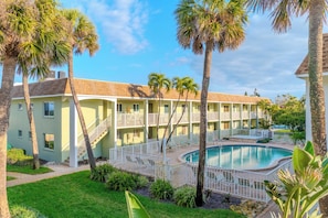 A motel with a swimming pool, multiple balconies, and palm trees. - Nautilus 207 by Nautilus Vacations-Beachfront Condo,Heated Pool,Recreation Court (Holmes Beach)