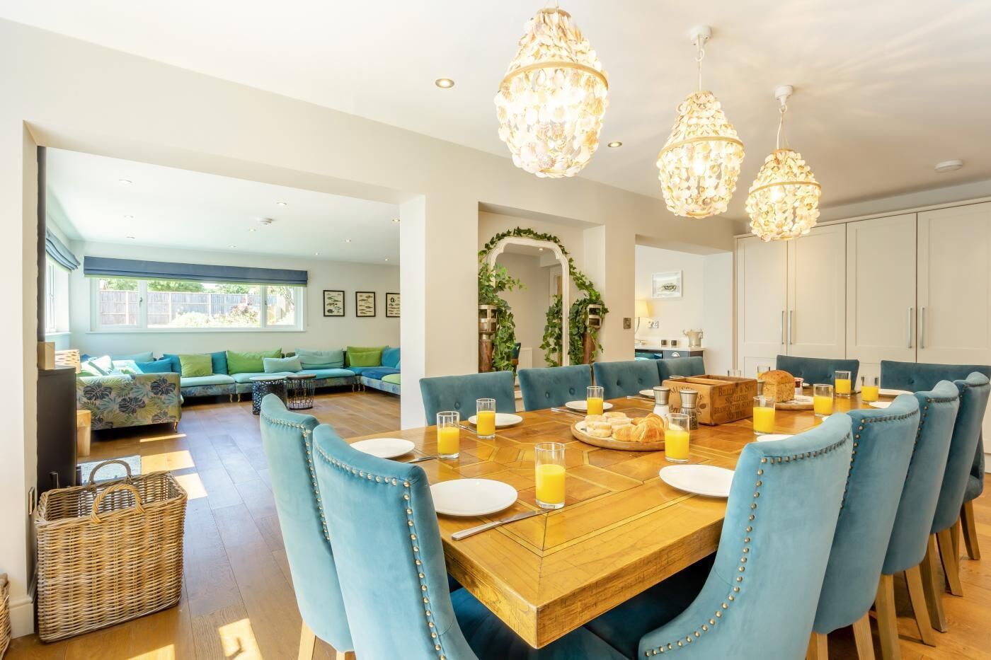 Un comedor con mesa de madera dispuesta para el desayuno, sillas tapizadas en azul y candelabros de cristal colgantes.