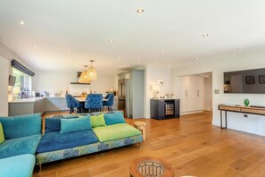 A modern living room with a sofa, a dining area with chairs, a kitchen with cabinets, and a TV mounted on the wall. - 6 Bed in Old Hunstanton (oc-a44903) (Hunstanton)