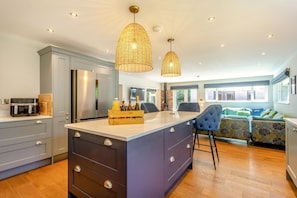 A modern kitchen with a central island, grey cabinets, and a blue upholstered sofa in the dining area. - 6 Bed in Old Hunstanton (oc-a44903) (Hunstanton)