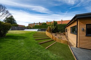 Ein gepflegter Garten mit einer Holzterrasse, die zu einem Haus mit Ziegeldach führt.