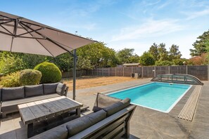 Un jardin avec une piscine, un patio couvert et un espace aménagé pour s’asseoir.
