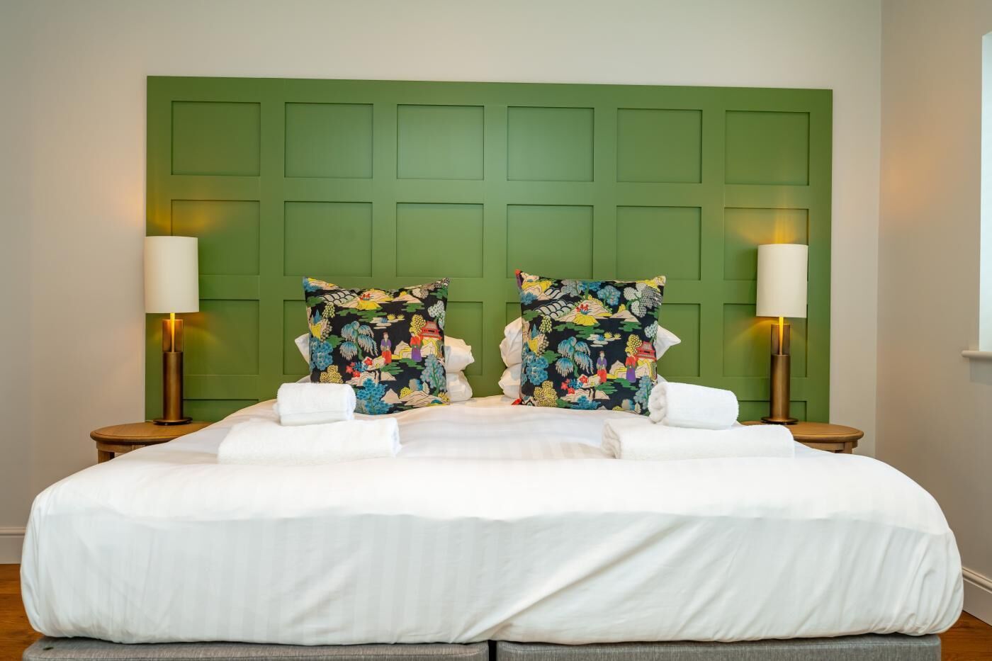 Een bed met witte lakens, twee sierkussens en twee bedlampjes.
