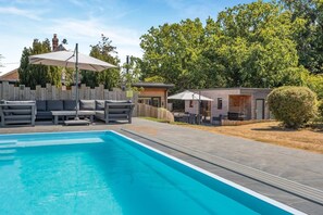 A swimming pool with a lounge area, a barbecue, and a small building, surrounded by trees and a wooden fence. - 6 Bed in Old Hunstanton (oc-a44903) (Hunstanton)