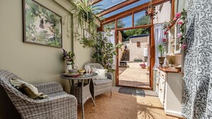 A sunlit room with wicker furniture, a glass door leading outside, and various plants. - 1 Bed in Appledore (oc-l45327) (Appledore)
