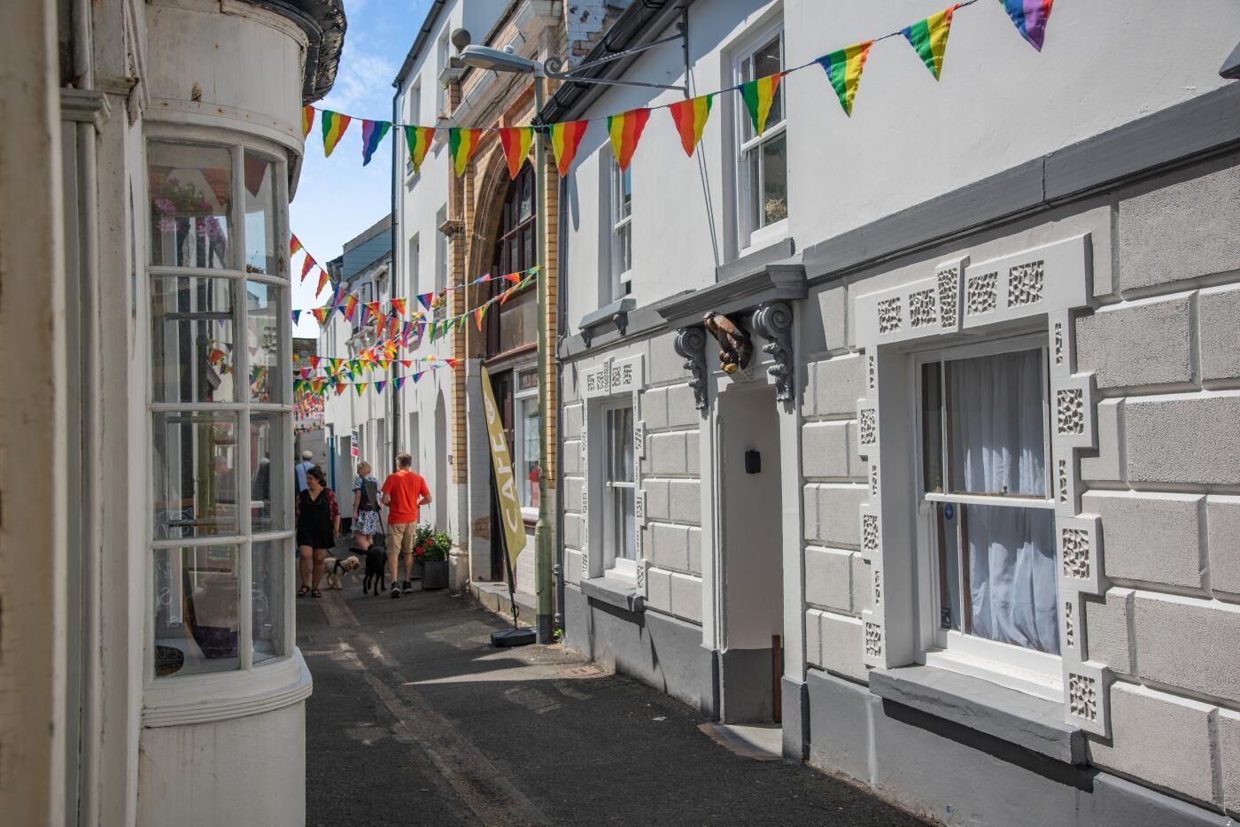 Une rue étroite, bordée de bâtiments des deux côtés, dont certains abritent des boutiques avec des devantures et des enseignes.