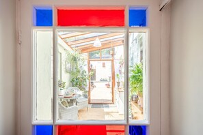 Ein Zimmer mit großem Fenster, einem Korbsessel, einem Tisch und mehreren Blumentöpfen.