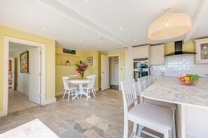 Een moderne keuken met witte kasten, een marmeren aanrechtblad en een eethoek met een witte tafel en stoelen.