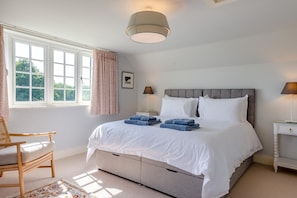 A bedroom with a bed, bedside tables, a chair, a window with curtains, and a hanging light fixture.