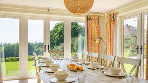 Un coin repas avec une table dressée pour quatre personnes, de grandes fenêtres et une vue sur la verdure.