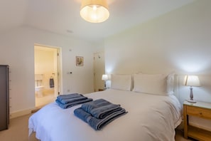 Een slaapkamer met een bed, twee bedlampen, een nachtkastje, een deur naar een badkamer en een kleine wanddecoratie.