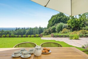 Une terrasse avec une table dressée pour le thé, entourée d’un jardin offrant une vue sur le paysage.