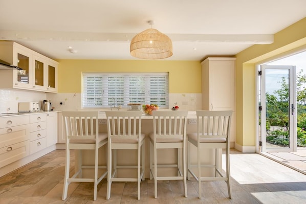 A modern kitchen with white cabinetry, a central island with chairs, a hanging light fixture, and a view through a glass door.