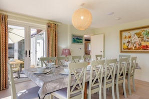 A dining area with a table set for four, chairs, a hanging light fixture, and a painting on the wall.