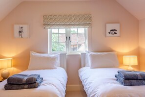 Une chambre avec deux lits, une fenêtre agrémentée d’une lambrequin à motifs et deux lampes fixées au mur.
