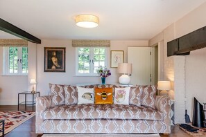 Un salón con un sofá estampado, un cuadro en la pared y una ventana con vistas a zonas verdes.
