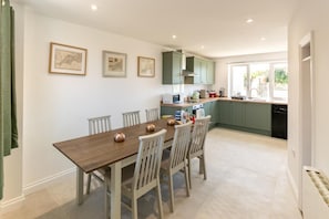 A modern kitchen with a dining area, featuring a wooden table, chairs, and green cabinets. - 3 Bed in Pendeen (oc-g33305) (Pendeen)