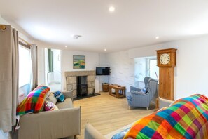 A living room with a fireplace, a television, a clock, and a sofa with colorful cushions. - 3 Bed in Pendeen (oc-g33305) (Pendeen)