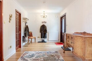 Un couloir avec un plancher en bois, un tapis rouge, une armoire en bois et un porte-manteau avec des vêtements.