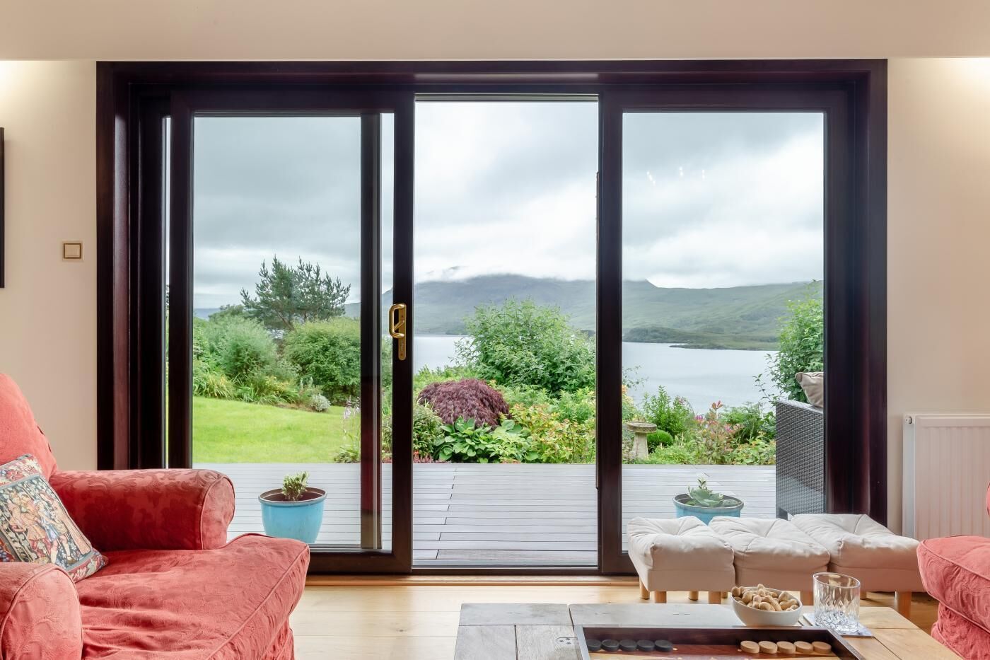 A room with a sliding glass door leading to a deck with a view of a lake and hills.