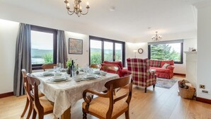 A dining area with a table set for four, a red sofa, and a view of the outdoors. - 3 Bed in Lairg (oc-r44959) (Little Assynt)