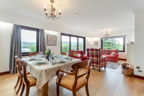 A dining area with a table set for four, a red sofa, and a view of the outdoors. - 3 Bed in Lairg (oc-r44959) (Little Assynt)