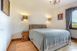 Ein Schlafzimmer mit einem Bett, Nachttischlampen, einem Nachttisch, einem Fenster mit Vorhängen und einer Kristallleuchter.