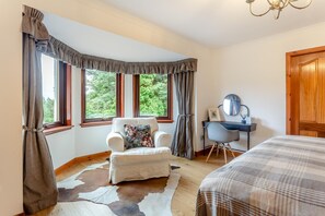 A bedroom with a large window, a white armchair with a floral pillow, a desk with a chair, and a bed with a striped blanket. - 3 Bed in Lairg (oc-r44959) (Little Assynt)