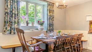 A dining area with a wooden table set for six, flanked by wooden chairs, a window with curtains, and a chandelier. - 5 Bed in George Nympton (oc-t40683) (George Nympton)
