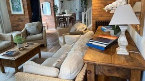 En hyggelig stue med sofa, stole, et sofabord og en lampe. I baggrunden er der et spiseområde med et bord og stole.