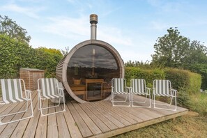 Eine Holzterrasse mit einer runden Struktur, möglicherweise eine Sauna, und vier gestreiften Stühlen.