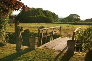 Eine Statue einer Frau in einem Feld mit einer Holzbrücke und einem Steinbau.