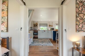 A narrow hallway leading to a kitchen with white cabinets, a microwave, and a window with a view of greenery. - 2 Bed in Overton (oc-k45280) (Overton)