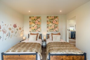 Ein Doppelzimmer mit zwei Betten, Blumenmotiv an der Wand und einer sichtbaren Küchenzeile.