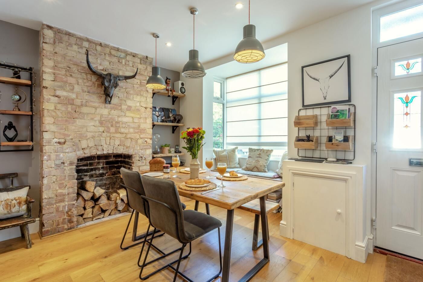 A cozy kitchen with a brick fireplace, wooden dining table, and modern pendant lights.