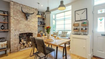 A cozy kitchen with a brick fireplace, wooden dining table, and modern pendant lights.
