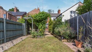 A residential backyard with a grassy lawn, a wooden fence, and various potted plants. - 2 Bed in Stamford (oc-m45276) (Stamford)
