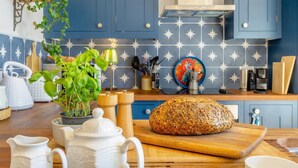 Een keuken met blauwe kastjes, een spatwand met sterrenprint, een brood met zaden op een houten plank, en diverse keukengerei.