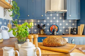 A kitchen with blue cabinets, a star-patterned backsplash, a loaf of seeded bread on a wooden board, and various kitchen utensils. - 2 Bed in Great Witchingham (oc-p45227) (Great Witchingham)