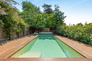 A rectangular swimming pool with a wooden deck surrounding it, set in a garden with various plants and a wooden fence. - 2 Bed in Great Witchingham (oc-p45227) (Great Witchingham)