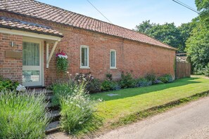Ein Ziegelhaus mit Ziegeldach, einer Haustür und einem kleinen Garten mit verschiedenen Pflanzen.