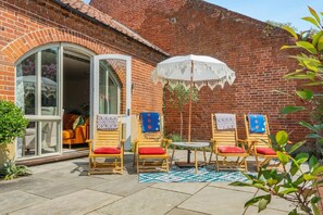 Eine Terrasse mit vier Holzstühlen, einem Tisch und einem weißen Sonnenschirm.