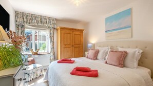 Een slaapkamer met een groot bed, een houten garderobe, een raam met gordijnen en een schilderij aan de muur.